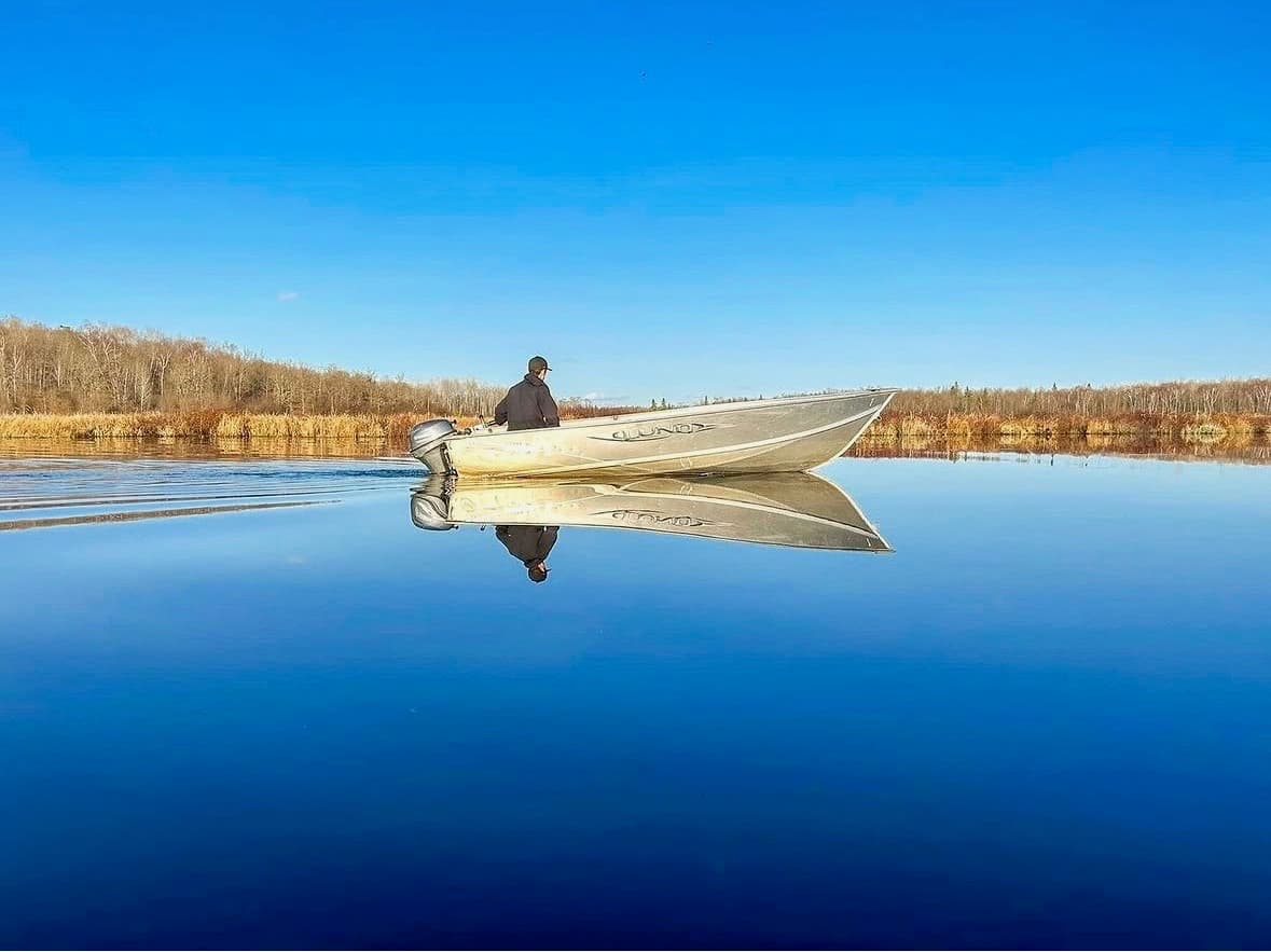 A lone fishing boat gliding across the glassy, mirror-still water of Betula Lake