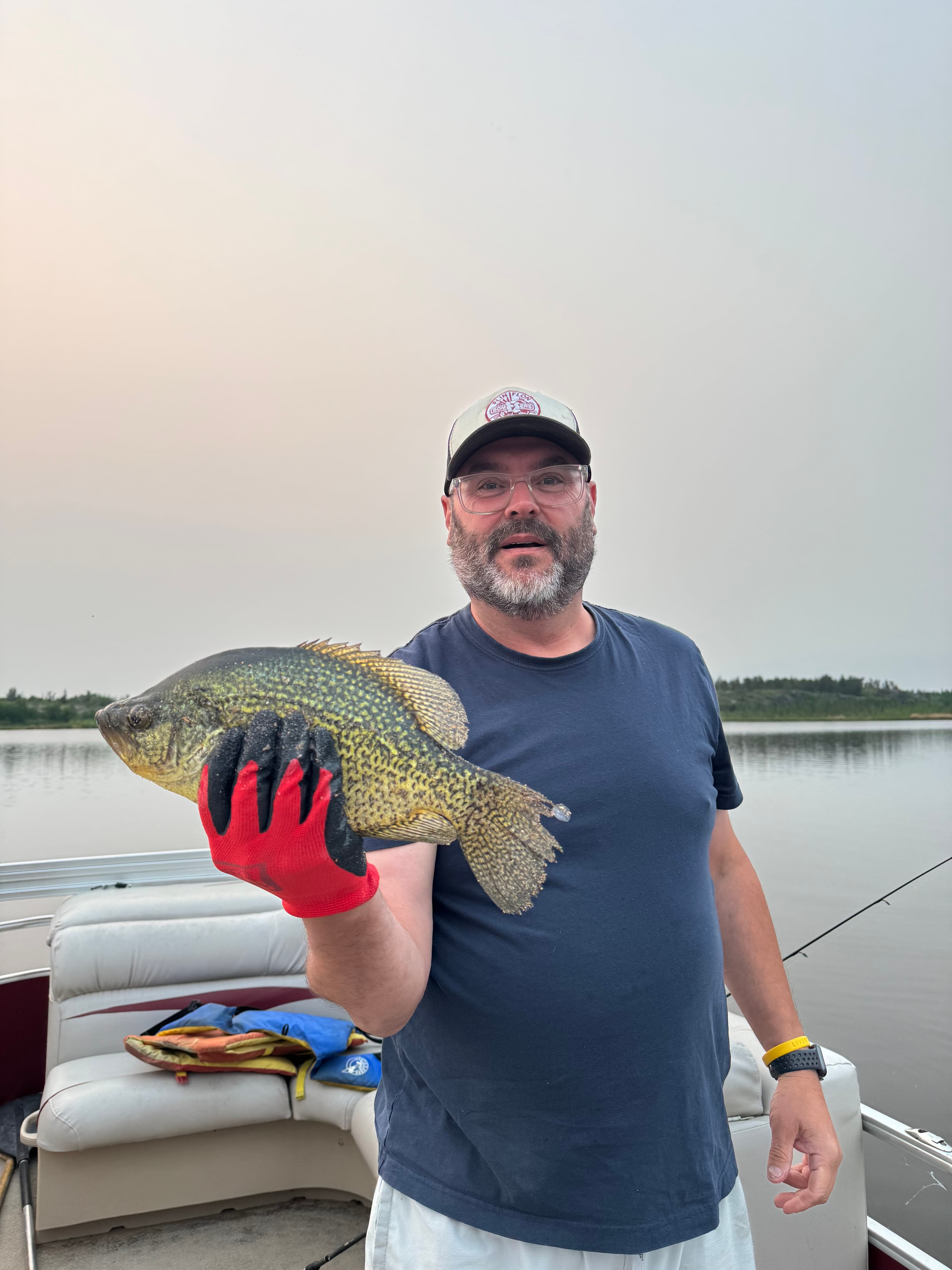 An angler holding up a freshly caught crappie on a boat at dusk on Betula Lake