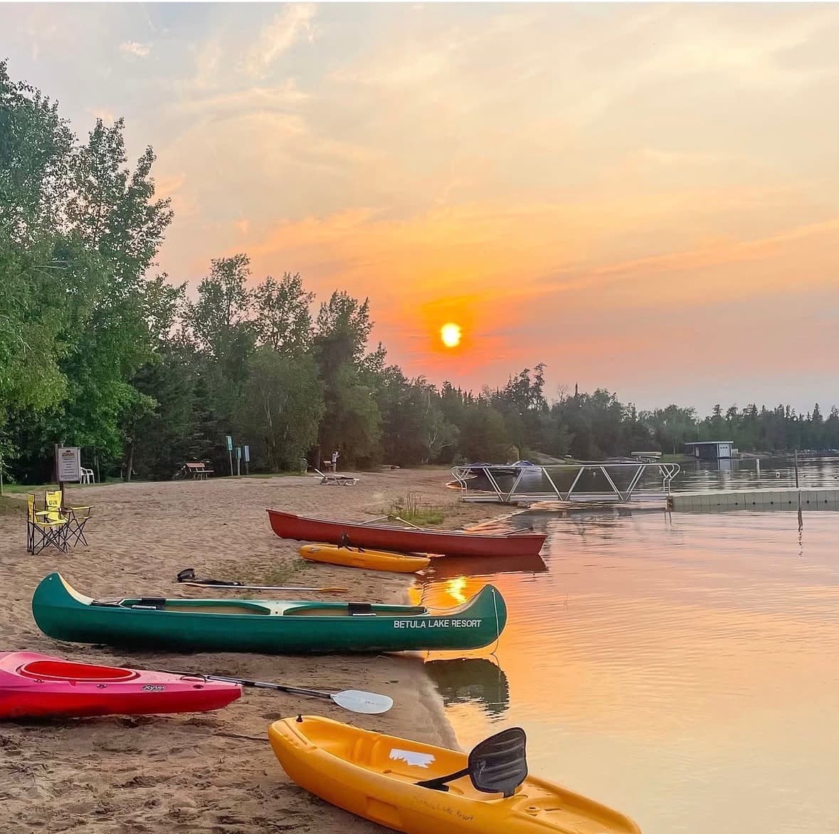 A canoe and kayaks pulled up on the sandy Betula Lake shore at sunset